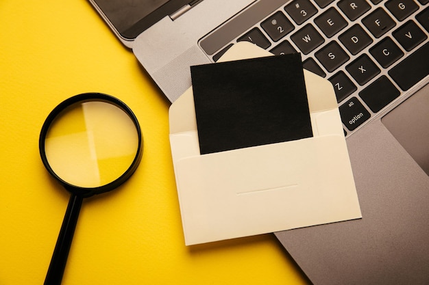 Paper envelope with card magnifier and laptop on a yellow background Top view