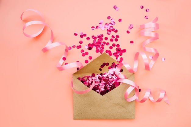 Paper envelope with pink confetti and ribbons