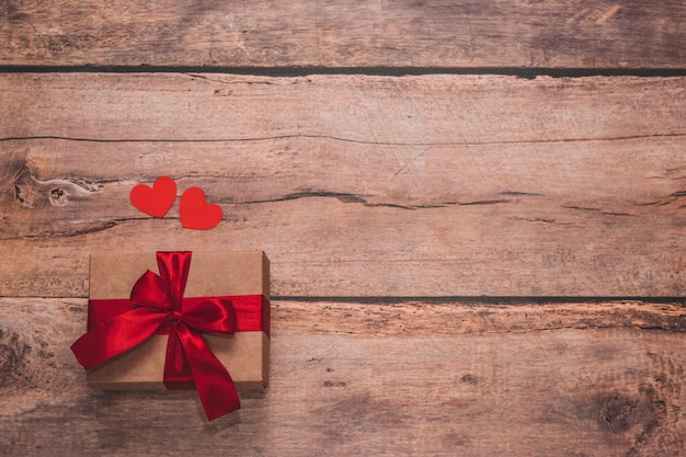 Paper hearts and a craft present with red ribbon on a wooden background. Top side angle view, flat lay. Valentines day concept. Copyspace.