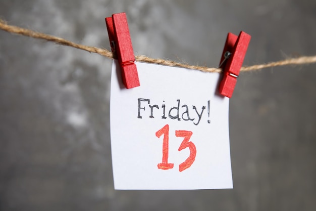 Paper note with phrase Friday 13 hanging on twine against grey background Bad luck superstition