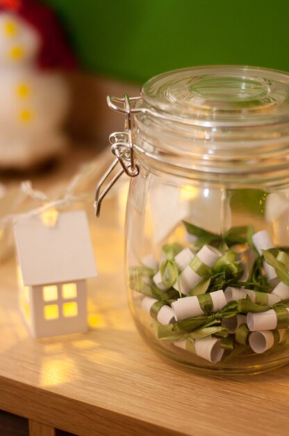 Paper notes with green ribbons in a glass jar on the background of Christmas lanterns