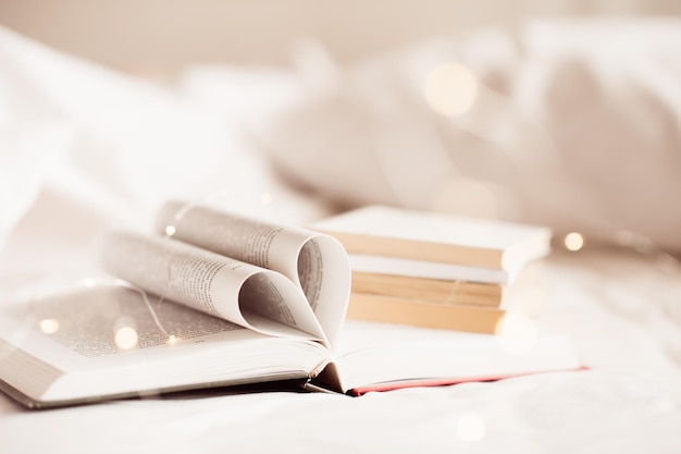 Paper open book with floded pages in heart shape in bed over glow lights and white background Cozy hygge atmosphere