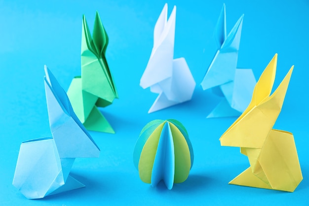 Paper origami Esater rabbits and colored eggs on a blue background. Easter celebration concept