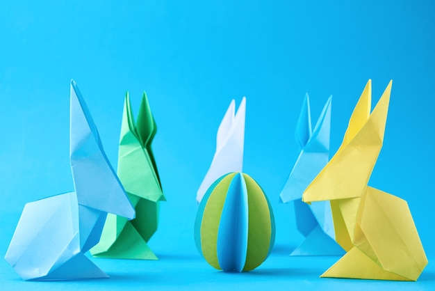 Paper origami Esater rabbits and colored eggs on blue wall. Easter celebration concept