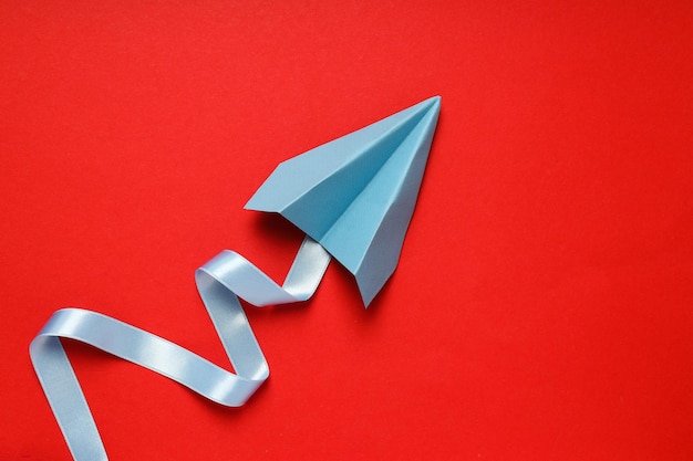 Paper plane with ribbon on red background