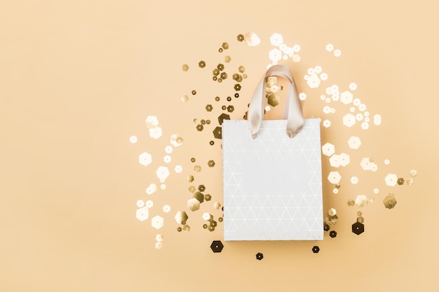 Paper shopping bag and trendy hexagonal sparkles on beige background Holiday sale concept in monochrome tones