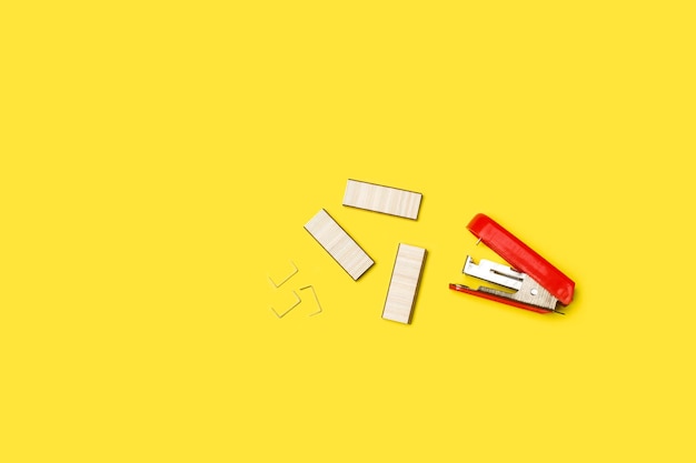 A paper stapler and staples on a yellow background with copy space