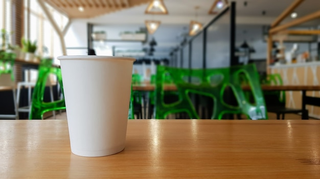 Paper white coffee cup disposable to take or go, on the wooden table of the coffee shop or dining room, place for a designer layout. Hot coffee cup in a cafe.