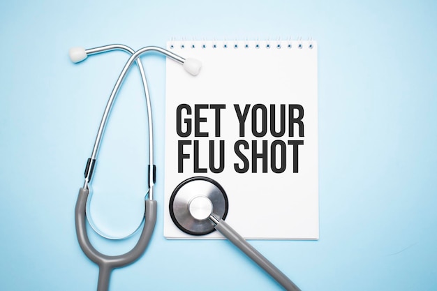 Paper with text get your flu shot on blue background with stethoscope and pills