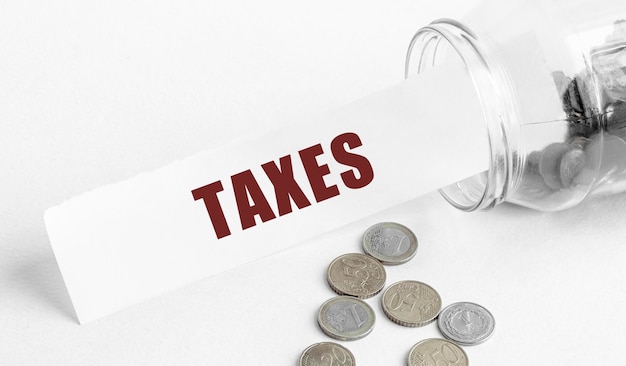 Paper with the text TAXES in a glass jar on a background of coins