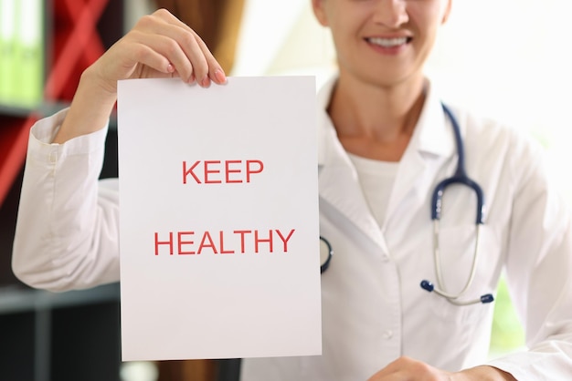 Paper with words keep healthy close up and female doctor with stethoscope in background