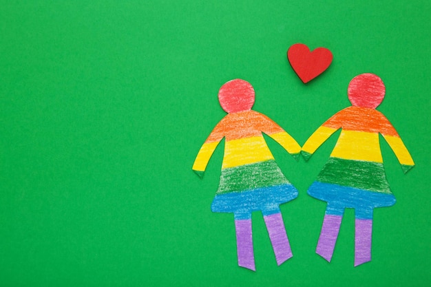 Paper women cut from paper and painted in LGBT colors with red heart Concept of LGBT on green Space for text