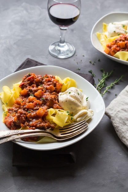 Pappardelle pasta with meat ragout and burrata cheese on gray concrete background. Italian cuisine.