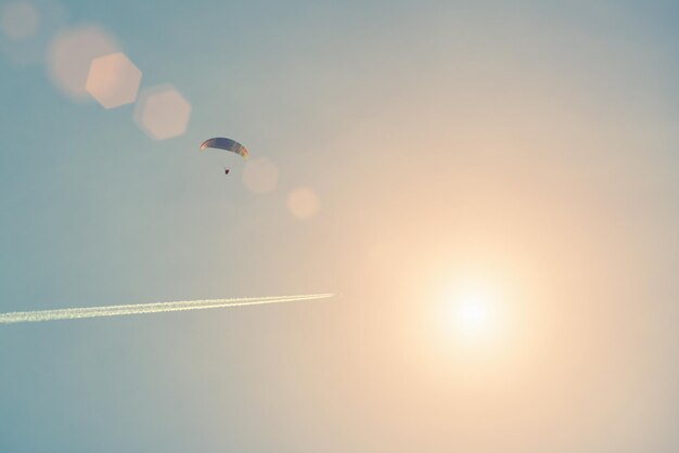 Paraglider in the sunny sky with a trace of an airplane