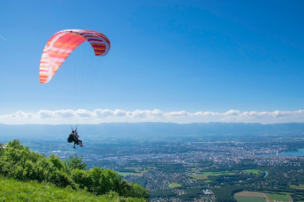 Paraglider with a red parachute is watching Geneva from air.