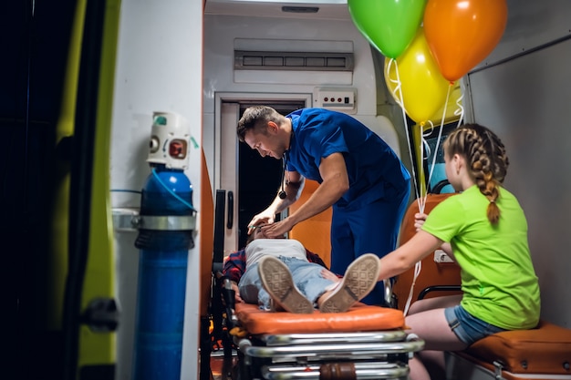 A paramedic in a blue medical uniform regulates an oxygen mask on a woman lying on a stretcher.