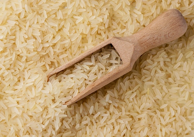 Parboiled rice with a wooden spoon closeup background Top view