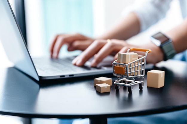 Parcel box in trolley on table with hand of young woman using laptop for shopping