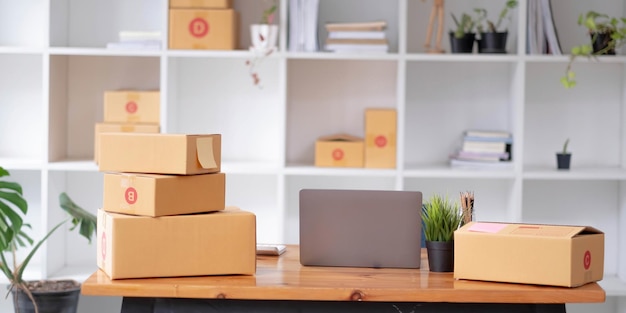 Parcel boxes on shelf and color shopping bags placing near laptop on table SME business on shopping online at home office packaging on background is popular business