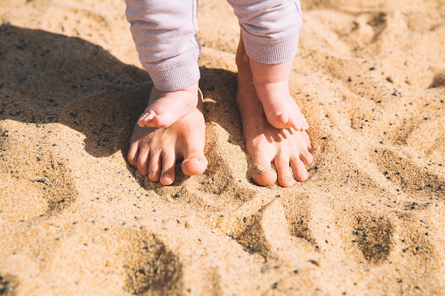 Parent and child walking barefoot Mother and cute little baby feet on summer beach sand