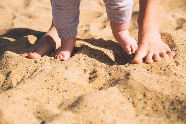 Parent and child walking barefoot Mother and cute little baby feet on summer beach sand