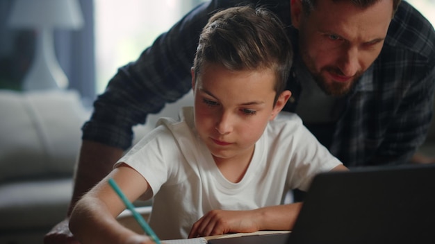 Parent helping child doing homework Smiling father son looking computer screen