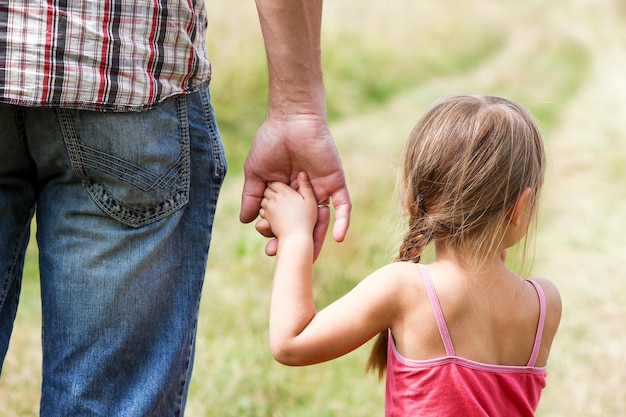 The parent holds the hand of a small child on nature