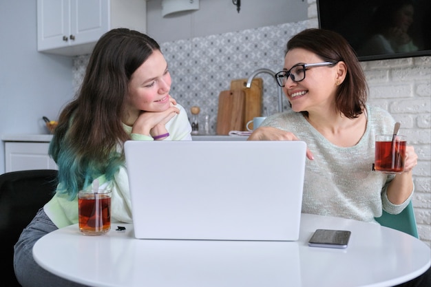 Parent and teenager sitting at home in kitchen and looking at laptop screen