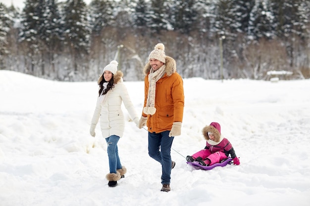 parenthood, fashion, season and people concept - happy family with child on sled walking in winter forest