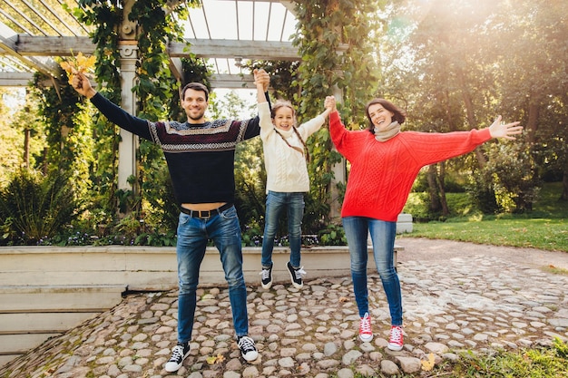 Parents and children concept Happy family have fun outdoors female and male play with little kid swing her in hands make gestures have wonderful relationship enjoy fresh autumn air