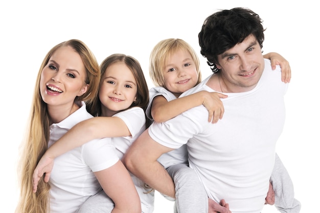 Parents giving two children piggyback rides smiling isolated on white wall