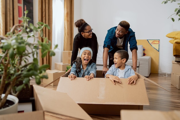 Parents have fun driving cute little son and beautiful daughter in cardboard box play in living room