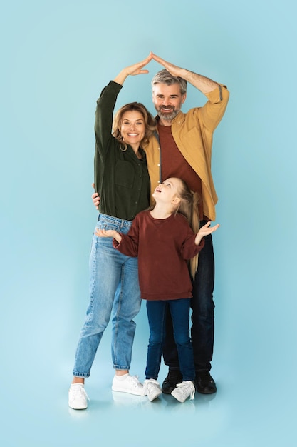 Parents joining arms making house roof above daughter blue background