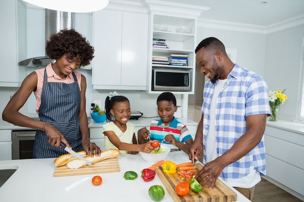 Parents and kids preparing salad while father using digital tablet in kitchen