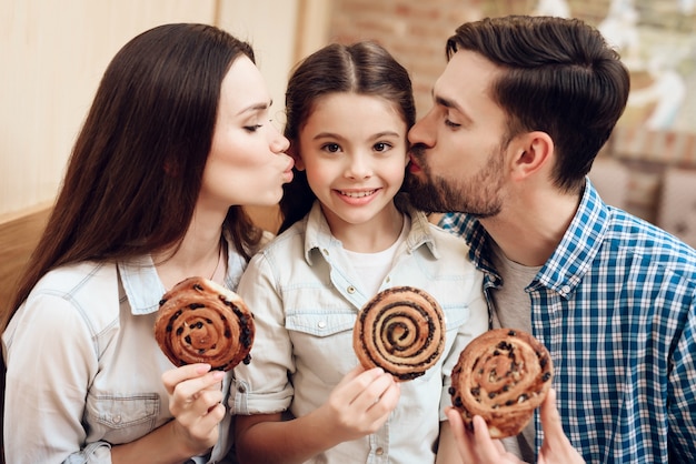 Parents kiss the girl on the cheek and eat buns.