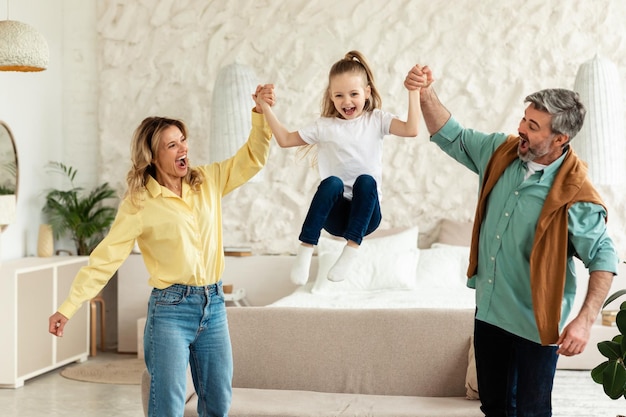 Parents playing with daughter holding hands while she jumping indoor