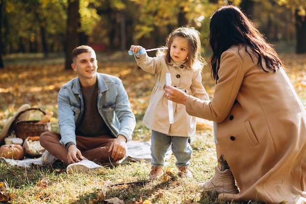 Parents playing with their daughter in soap bubbles in the autumn park