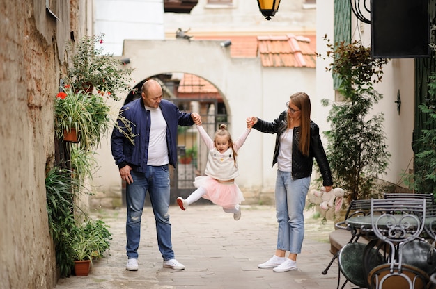 Parents raised and hold the little daughter by the hands. Girl having fun and waving legs.