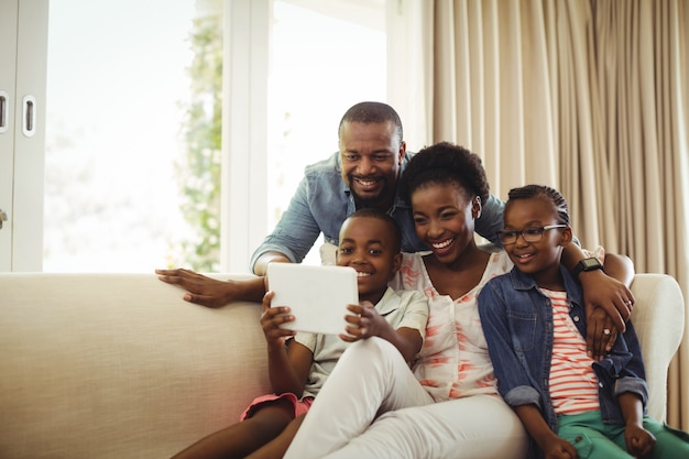 Parents and son using digital tablet on sofa in living room