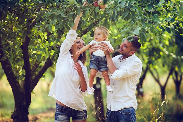 Parents with baby enjoying picnic on a farm with apple and cherry trees.