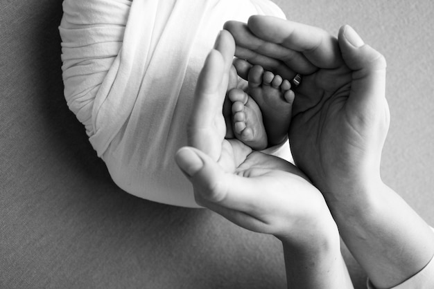 Parents39 palms Father and mother hold the legs of a newborn baby Feet of a newborn in the hands of parents Photo of the foot heels and toes Black and white studio macro shot