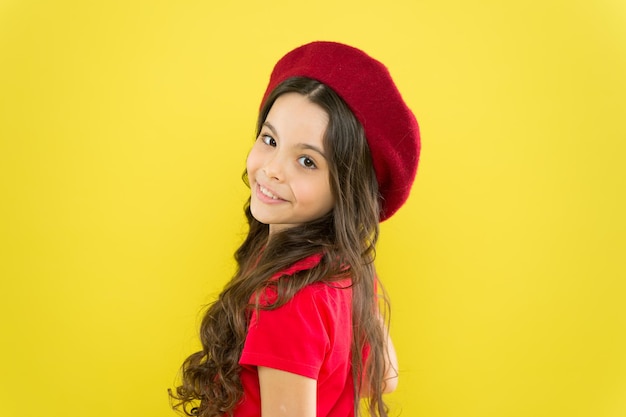 Parisian child on yellow background summer fashion and beauty little girl in french style hat happy girl with long curly hair in beret childhood hairdresser salon Cosmetology and beauty