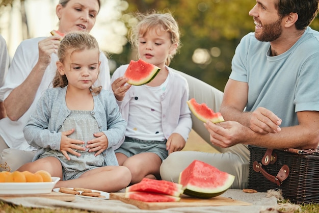 Park picnic and couple with children and fruit on blanket in garden for happy summer family time together Nature love and relax eating lunch on grass with parents and kids with smile on holiday