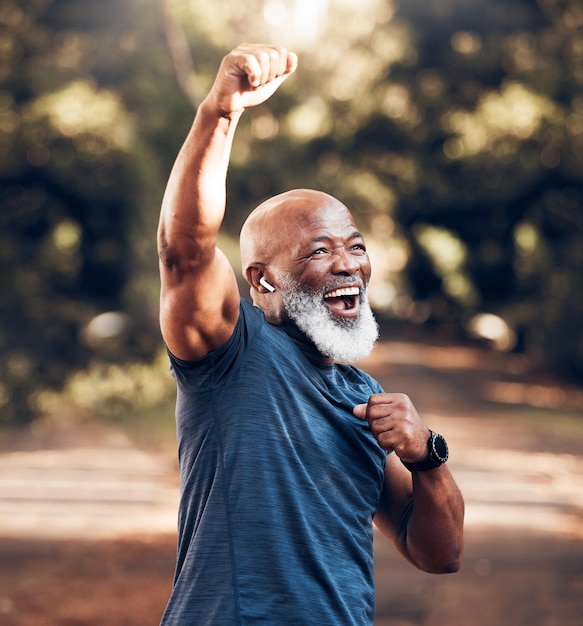 Park success and running winning black man excited and celebration at fitness run in nature with earphones Music workout and mature runner with smile and happy to celebrate exercise achievement