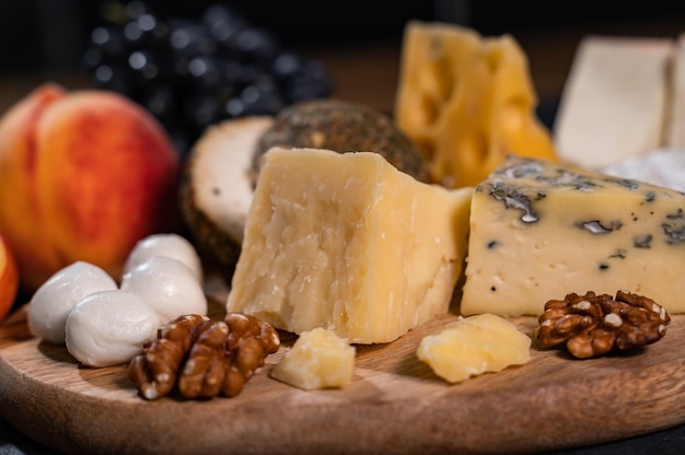 Parmesan and walnuts on a wooden board. In the background mozzarella, peaches, grapes.