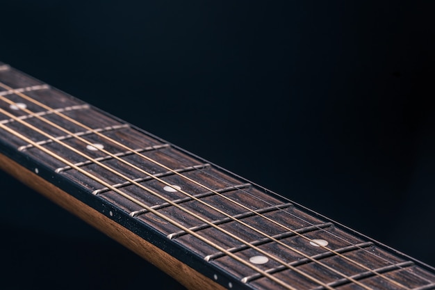 Part of an acoustic guitar, guitar fretboard on a black background.