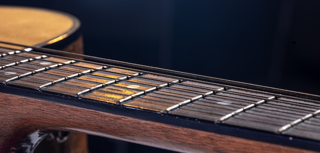 Part of an acoustic guitar, guitar fretboard with strings on a black background with highlights.