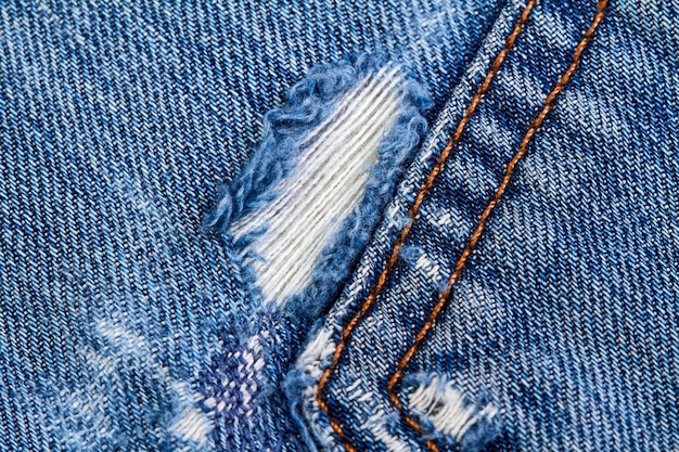 Part of a blue denim jeans background pocket with damage and seams with orange thread stitches