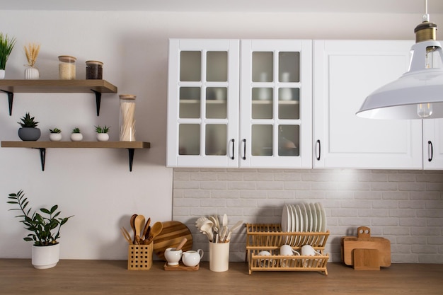 Part of the interior of a white modern kitchen with cabinets with frosted glass, a brick white wall and a wooden countertop. kitchen equipment.