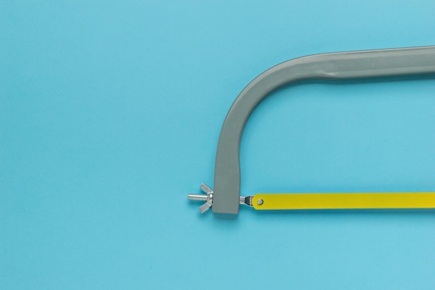 Part of a metal hacksaw with a yellow blade on a blue background Minimal concept of a hand tool Flat lay